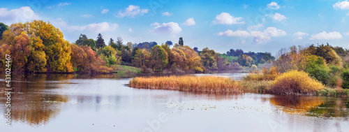 Autumn landscape with colorful trees by the river and picturesque blue sky with white clouds, panorama