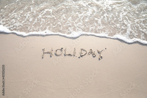 The word "HOLIDAY" written in the sand in capital letters.