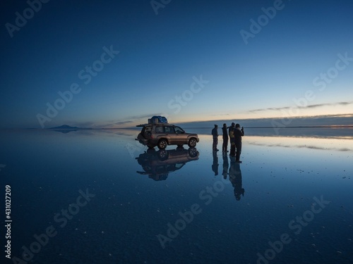 Tourist group with offroad car SUV on Salar de Uyuni salt flat lake in Bolivia andes mountains sunrise mirror reflection