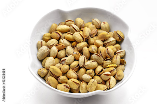 A white bowl with a bunch of salted and roasted pistachio seeds on a white background. Perfect shot for vegan diet,.