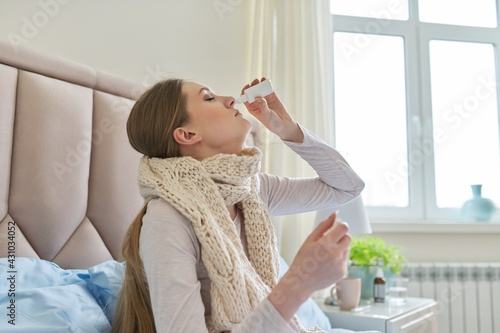 Young sick woman sitting in bed with nose drops and handkerchief