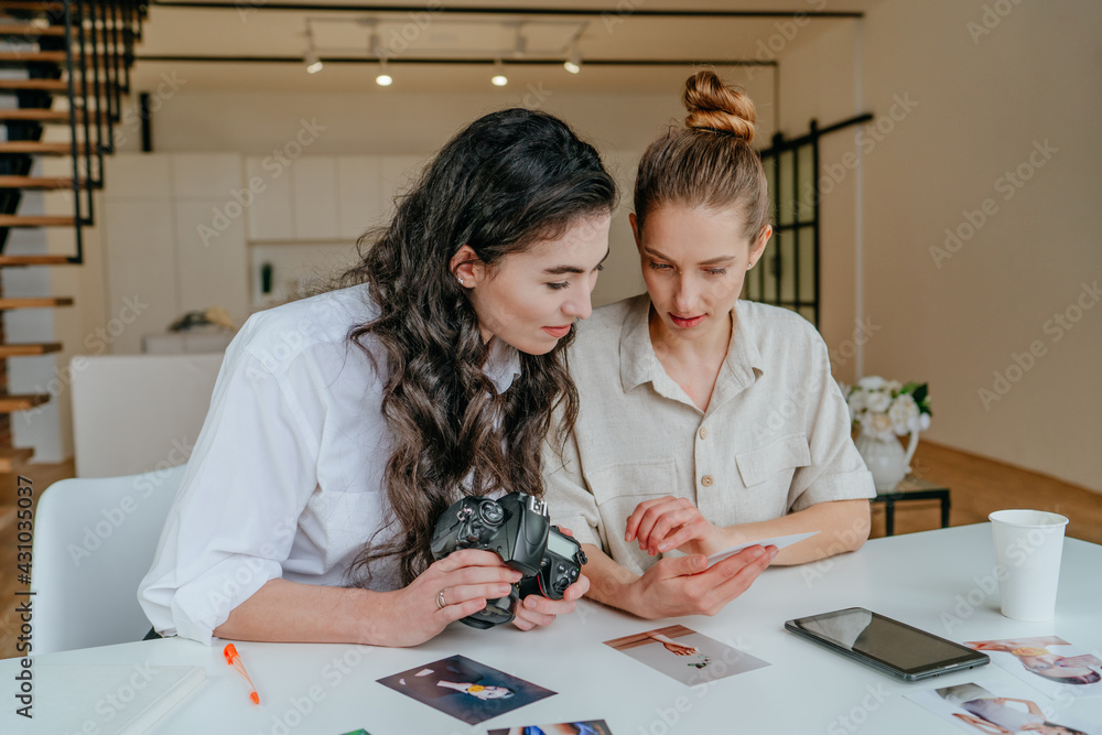 Two young women selecting photos on the camera indoor
