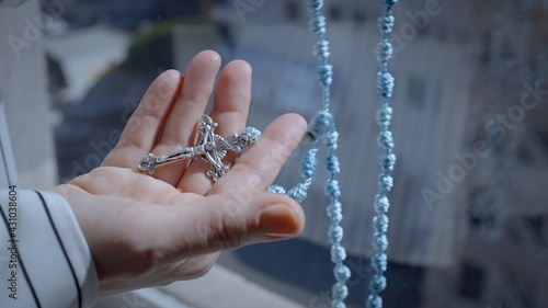 Tilt from close on hand holding crucifix to woman's hand counting through knots on a blue string rosary with blue sky in background