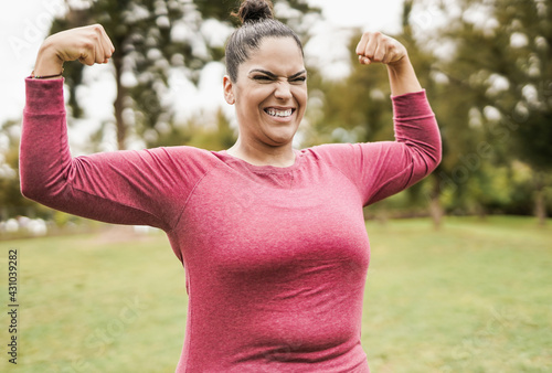 Plus size woman at city park posing showing biceps muscles - Curvy girl after sport workout outdoor