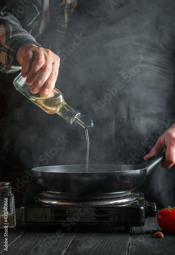 Cook or chef adds olive oil to the pan while cooking. Working environment on the restaurant kitchen table. Vertical image