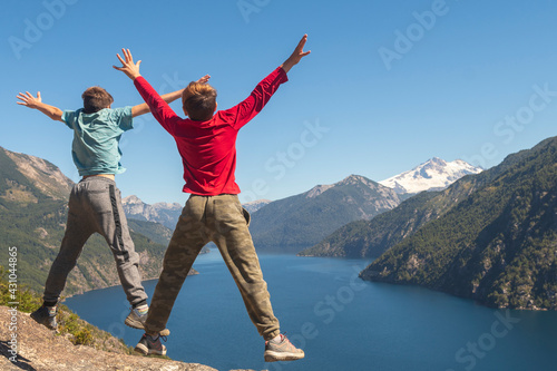 Two children jumping for joy into the abyss of the rock with the background of the Andes Mountains in Patagonia.