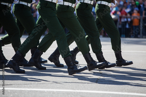 a solemn parade in the city square during a military holiday, the best soldiers marching synchronously in a column of systems, stamping step with weapons in hand, demonstration of military power