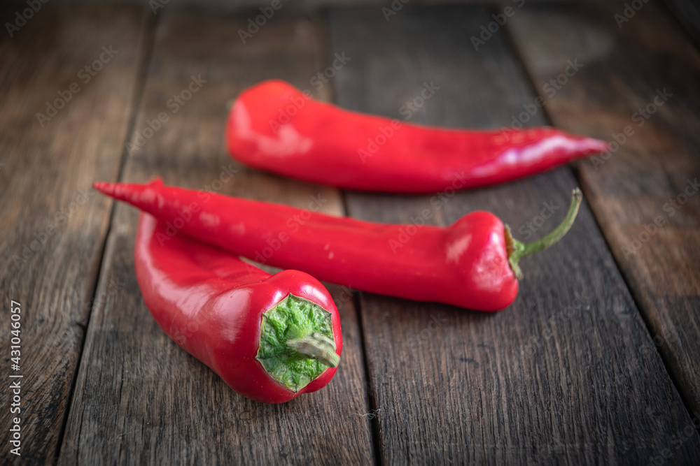 Three appetizing red peppers lie on a wooden kitchen table.