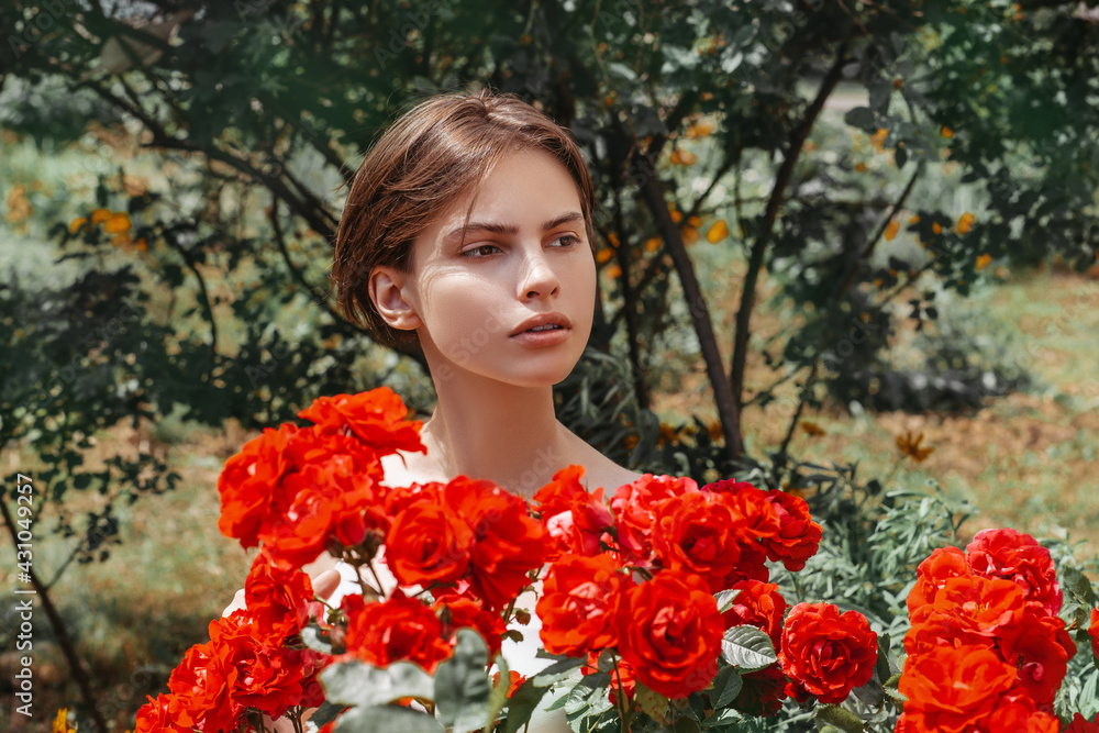 Naklejka premium Beautiful girl behind a blooming red rose bush