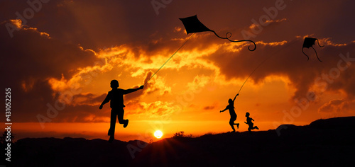 Sylwetki dzieci puszczających latawca o zachodzie słońca