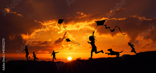 Sylwetki dzieci puszczających latawce o zachodzie słońca