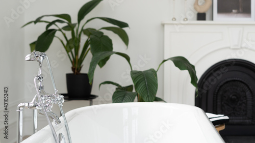 Silver showerhead and faucet on white bathtub against fireplace