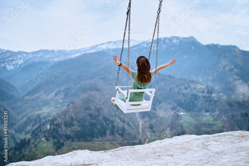 Free woman traveler with open arms enjoying of swinging on a heavenly swing and mountain view. Calm and quiet wanderlust concept moment when person feels happiness and freedom