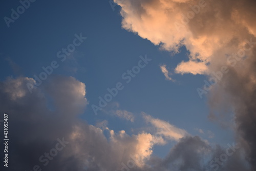 Dark rain clouds on a background of dark blue sky, illuminated by the sun to orange. Atmospheric phenomena