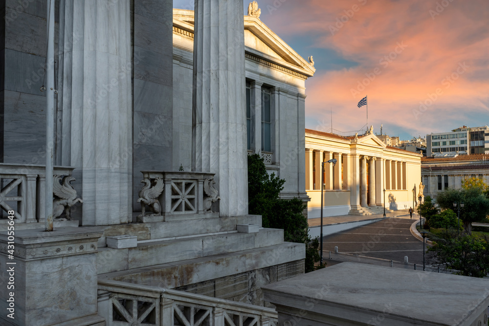 Obraz premium Athens, Atica, Greece - Oct 23, 2020: The University of Athens neoclassical building as seen from the National Library of Greece neoclassical building in the center of Athens city. Sunset time
