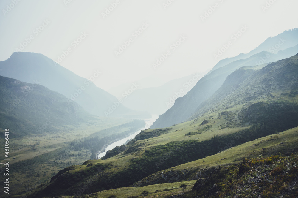 Misty mountain landscape with hills and rocks on background of wide mountain river in mist. Atmospheric scenery with mountain relief and big river in dark green valley in rainy weather. Gloomy weather Misty mountain landscape with hills and rocks on background of wide mountain river in mist. Atmospheric scenery with mountain relief and big river in dark green valley in rainy weather. Gloomy weather