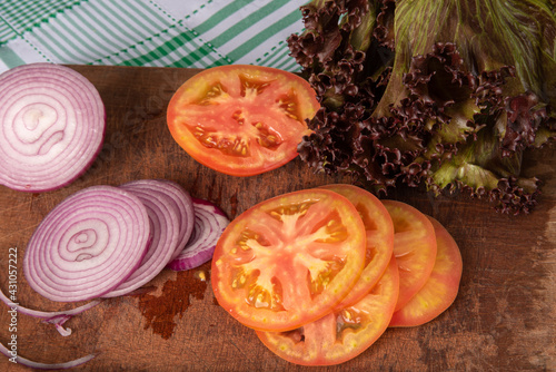 tomatoes, red onion and red lettuce in detail on wood over checkered tablecloth, selective focus.