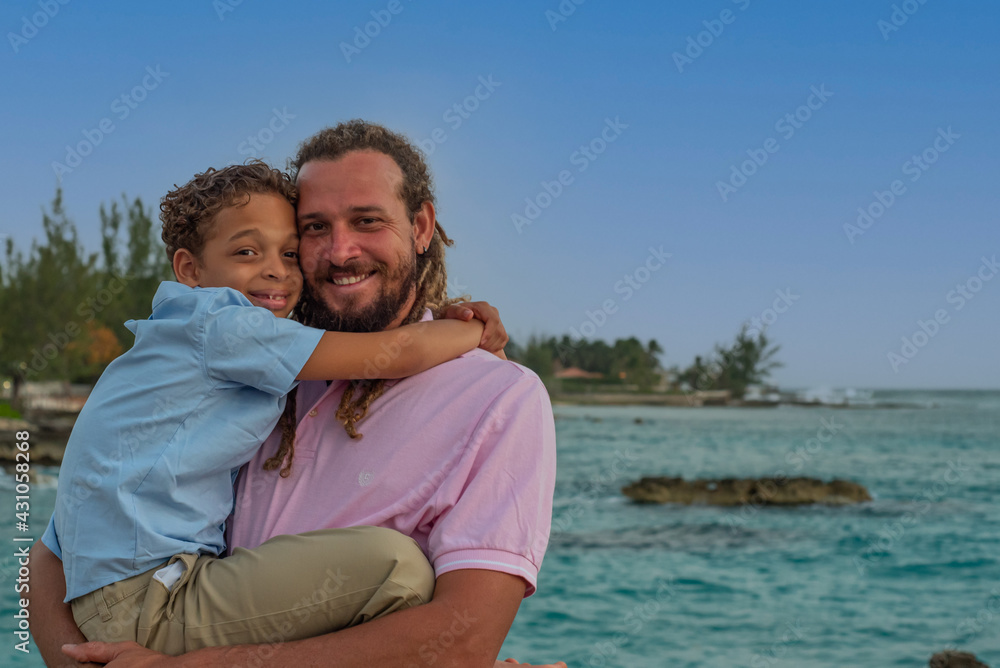 A mixed race father and son. The modern dad has dreadlocks and the pair are enjoying an awesome day at the beach A mixed race father and son. The modern dad has dreadlocks and the pair are enjoying an awesome day at the beach
