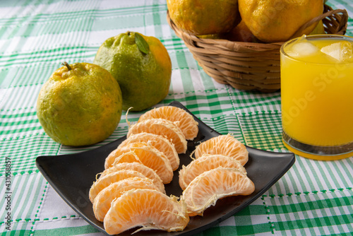 Orange ponkan, orange ponkan slices on a black plate, plus some oranges and a glass of juice on a checkered tablecloth on a light background, selective focus. photo