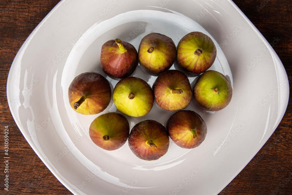 Purple figs, purple figs on a white plate on rustic wood, black background, top view. Purple figs, purple figs on a white plate on rustic wood, black background, top view.