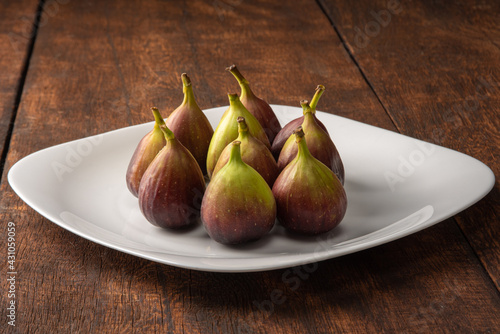 Purple figs, purple figs on a white plate on rustic wood, black background, selective focus.