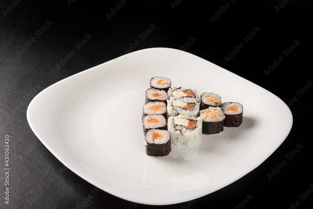 Sushi, beautiful arrangement of sushi made on a white plate on dark surface, black background, selective focus. Sushi, beautiful arrangement of sushi made on a white plate on dark surface, black background, selective focus.