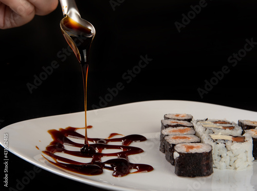 Schilderij op canvas Sushi, beautiful sushi arrangement decorated with tare sauce on a white plate on a dark surface, black background, selective focus
