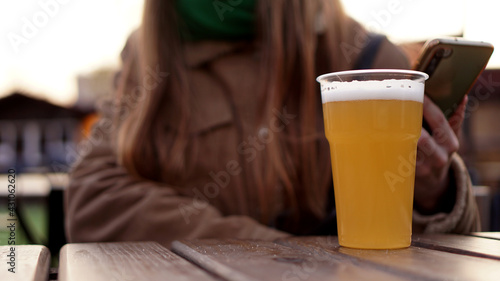 Light beer in a plastic glass. Girl drinking beer at the food court - blurred background