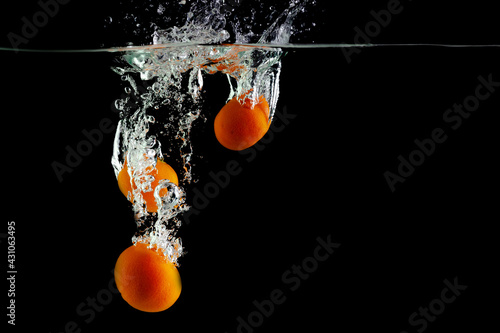 three tangerines fall into the water on a black background