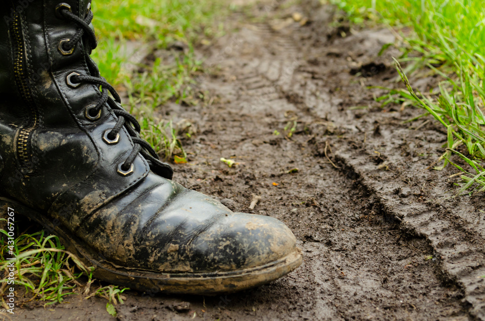 The feet of a man in boots on muddy country road. Dirty ground. Dirty army boots walking on the rainy road. Spring. Autumn. The feet of a man in boots on muddy country road. Dirty ground. Dirty army boots walking on the rainy road. Spring. Autumn.