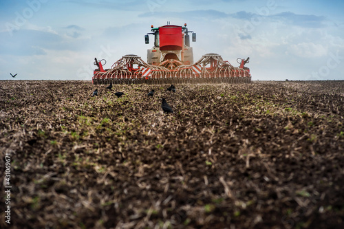 Farmers sow, tractor with a seeder in a plowed field