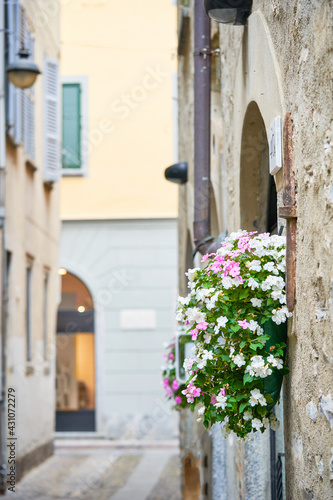 Flower pot hanging on wall, narrow cosy italian street in small town in Lombardy, North Italy, Europe. Decorative pot with flowers