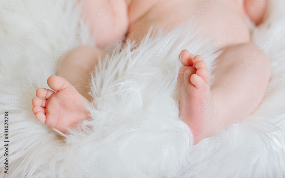 Newborn baby infant laying at white soft fur fluffy blanket, tiny feet toes close up, family love concept, light tones Newborn baby infant laying at white soft fur fluffy blanket, tiny feet toes close up, family love concept, light tones