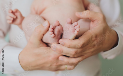 Father man hands hold tiny feet toes of newborn infant baby, tender light neutral colors, beautiful family and dad love