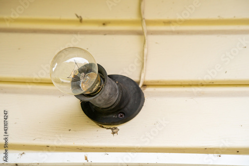 An incandescent light bulb with cobwebs and dirt illuminates the white wall in the entrance of the house. The beginning of the summer cottage season