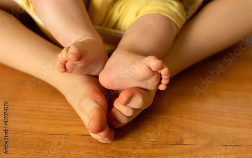 Infant baby girl sit on legs of older sister, loving family concept, barefoot kids at wooden home floor