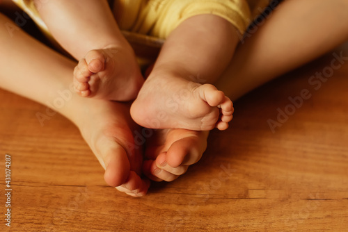 Two girls sisters differetn age sit together barefoot on wooden floor, tiny baby feet toes, family love concept