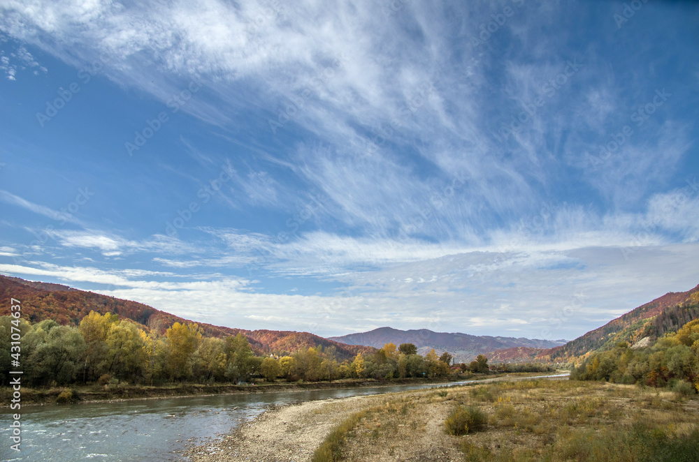 A river among the mountains with colorful autumn foliage and a bright sky.