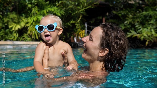 Happy childhood concept. Young Caucasian mom plays with her cheerful baby in the swimming pool 