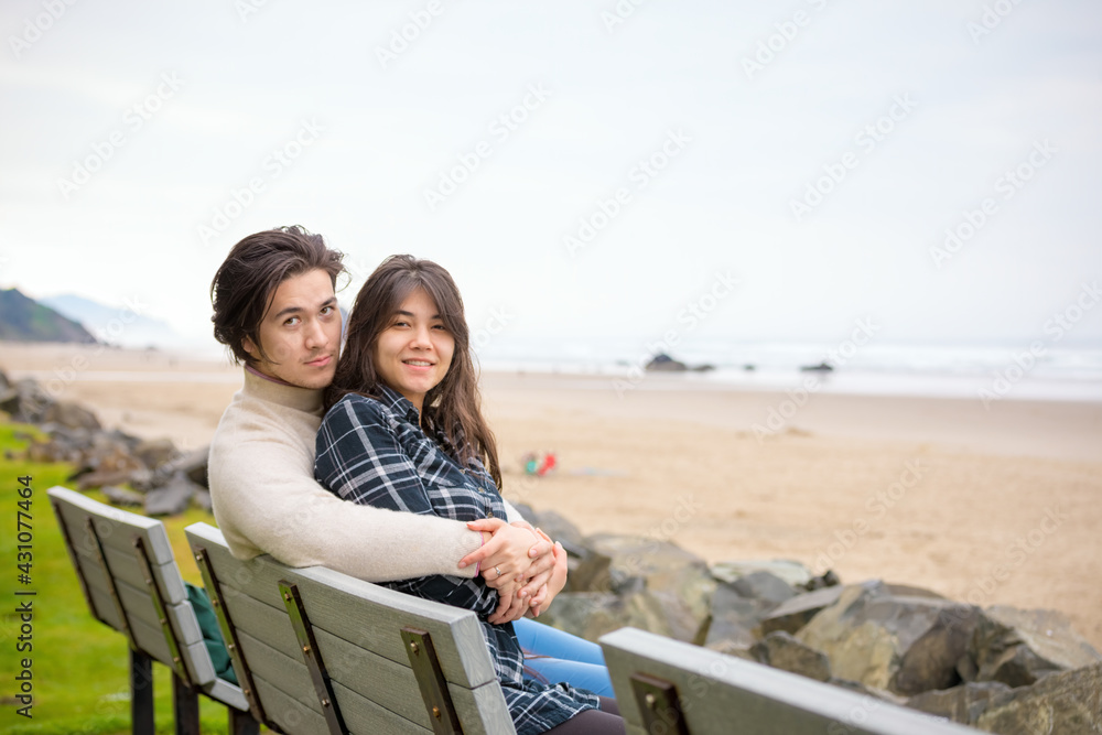 Young biracial couple sitting together on bench by the ocean