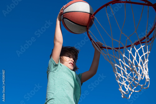 Kid basketball player makes slam dunk. Active child enjoying outdoor game with basketball.