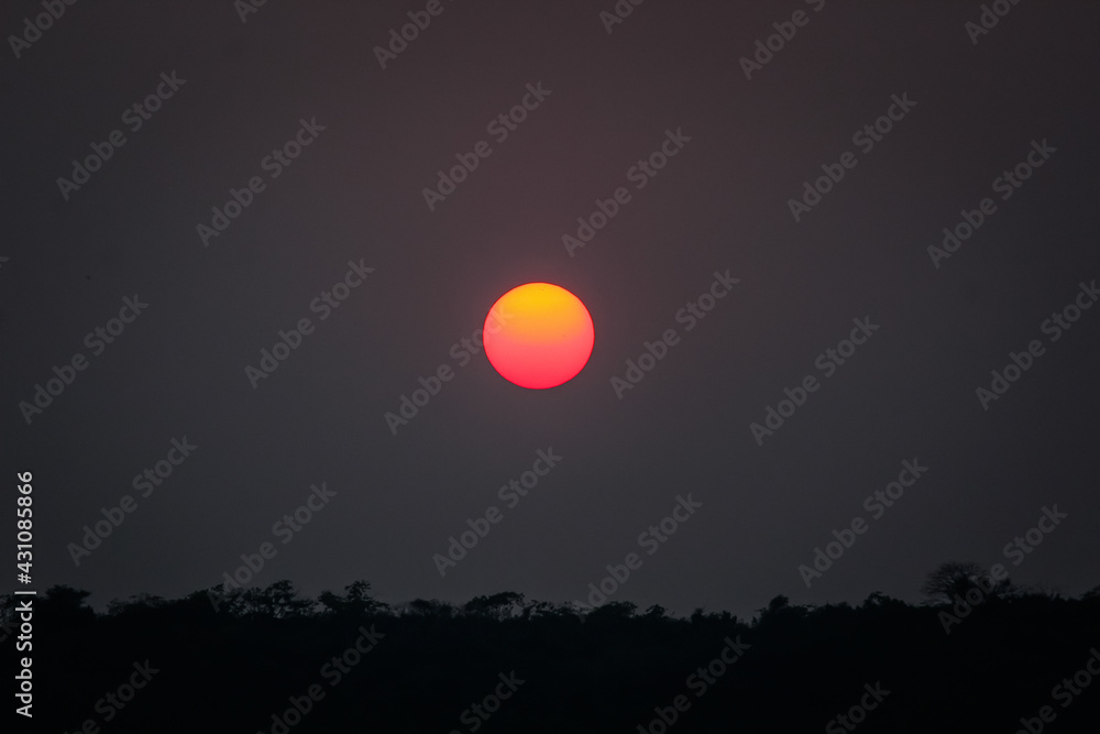 The evening view of the sunset where the sun is completely round and filled with yellow and orange colors. The evening view of the sunset where the sun is completely round and filled with yellow and orange colors.