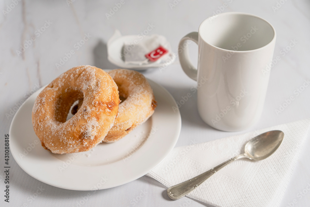 Pair of donuts with sugar and filled with sweet on a white plate with a white cup on a marble table. Pair of donuts with sugar and filled with sweet on a white plate with a white cup on a marble table.