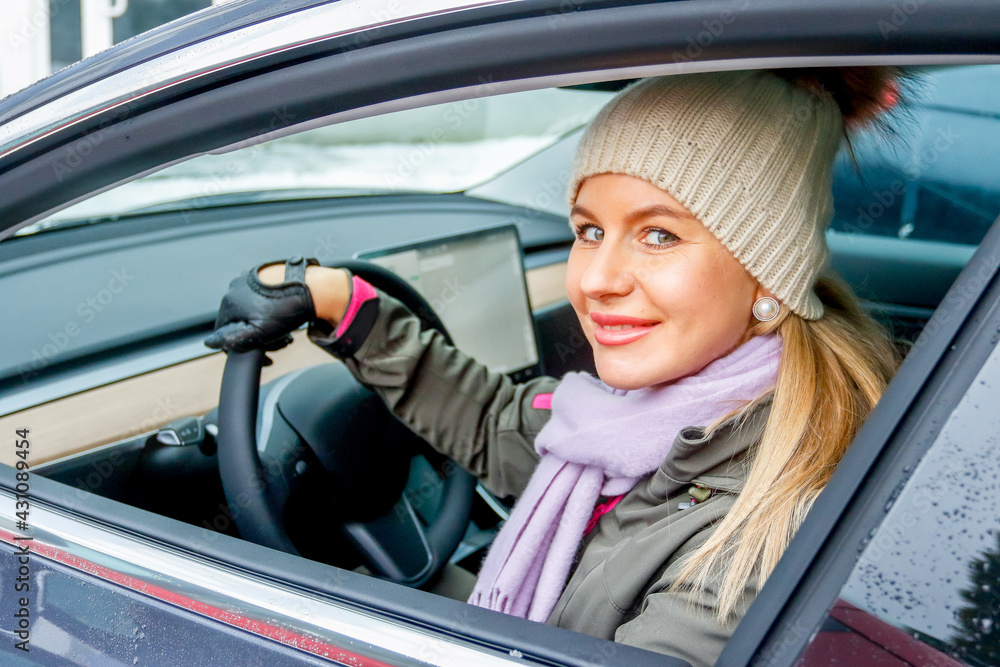 MINSK. BELARUS - JANUARY 2021: Beautiful woman looks out the window of an electric car. MINSK. BELARUS - JANUARY 2021: Beautiful woman looks out the window of an electric car.