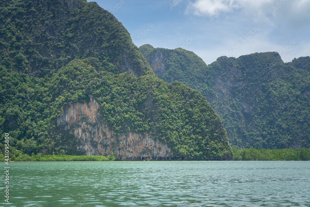 View of limestone island with high cliff in blue sky enrivonment and turquoise sea as foreground. Nature and outdoor scenic photo.