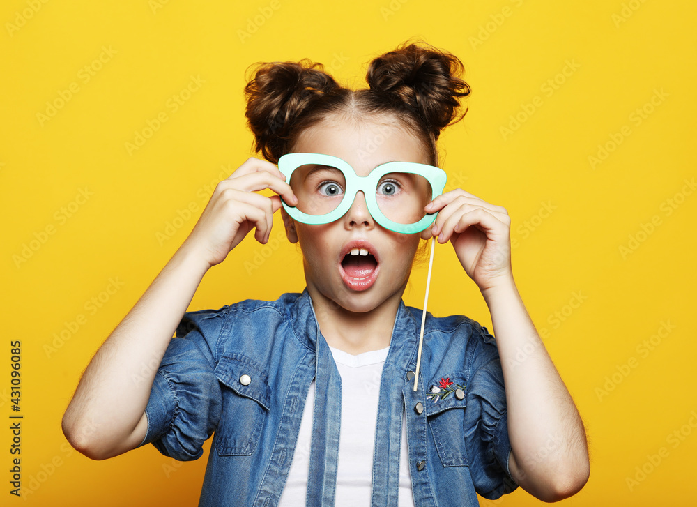 Party, childhood and people concept: little girl with a paper carnival accessories over yellow background. Party, childhood and people concept: little girl with a paper carnival accessories over yellow background.