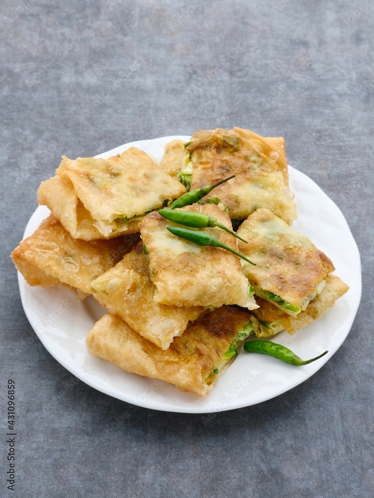 Martabak, Martabak Telor or Martabak Telur. Savory pan-fried pastry stuffed with egg, meat and spices. Martabak Telur is one of Indonesia street food. Served on white plate on grey background. Martabak, Martabak Telor or Martabak Telur. Savory pan-fried pastry stuffed with egg, meat and spices. Martabak Telur is one of Indonesia street food. Served on white plate on grey background.