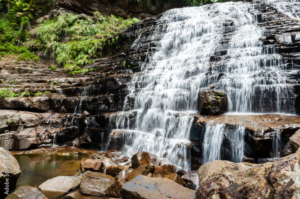 Obraz premium Mayagusuku waterfall in the middle of the jungle on the island of Iriomote with its formation in stones ladder and its waters flowing over them.