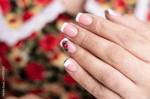 Manicure. White French jacket and red flower design gel paints on the nails of a young girl. Nail care in a beauty salon. Close-up