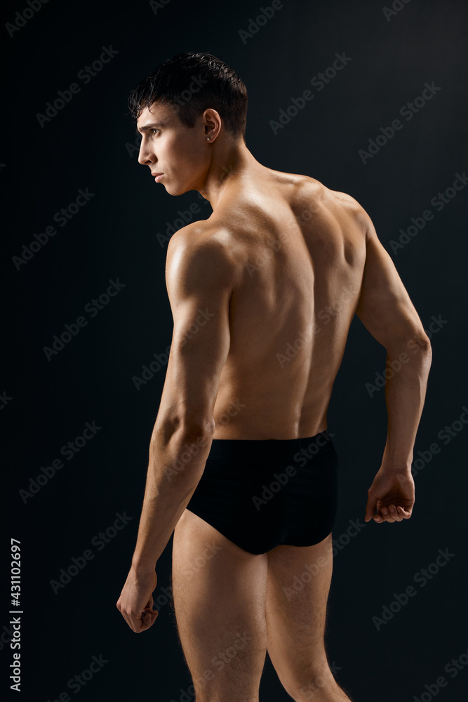 a handsome man bodybuilder with a pumped-up body stands with his back dark background